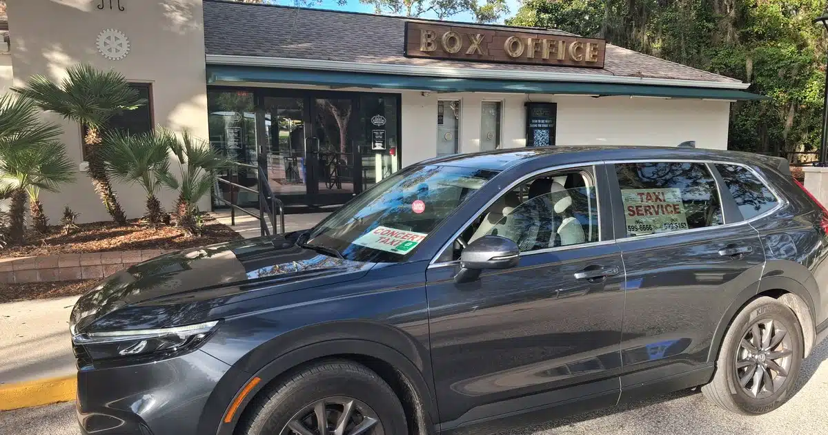 abraxi-taxi-st-augustine-social-1200x630 Black SUV taxi parked in front of a Box Office storefront with signs reading Taxi Service and Concierge Taxi in the windows.